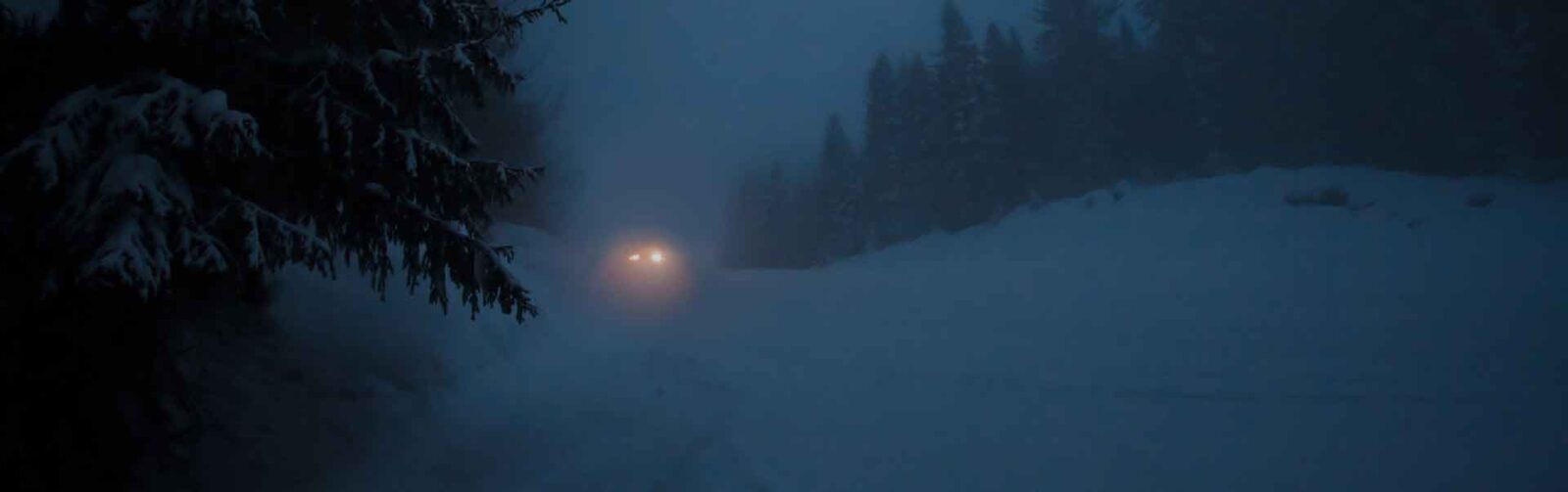 oncoming lights of vehicle driving in dark and snowy conditions
