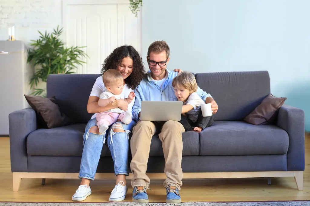 two parents and two young children sit on a couch with a laptop