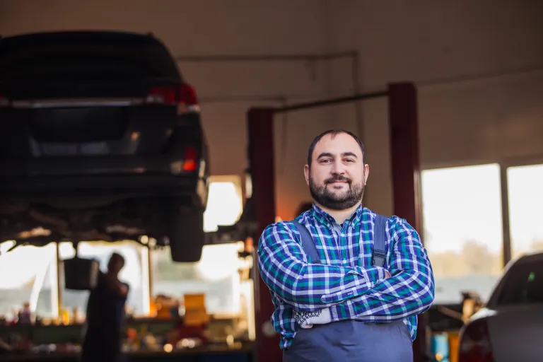 man standing with his arms crossed in front of a car on a hoist