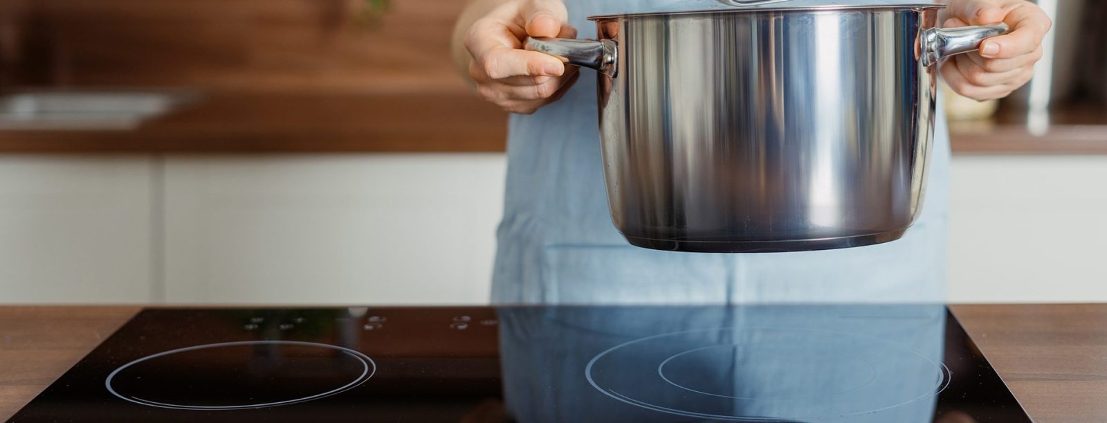 A pair of hands holding a pot over an induction stove top