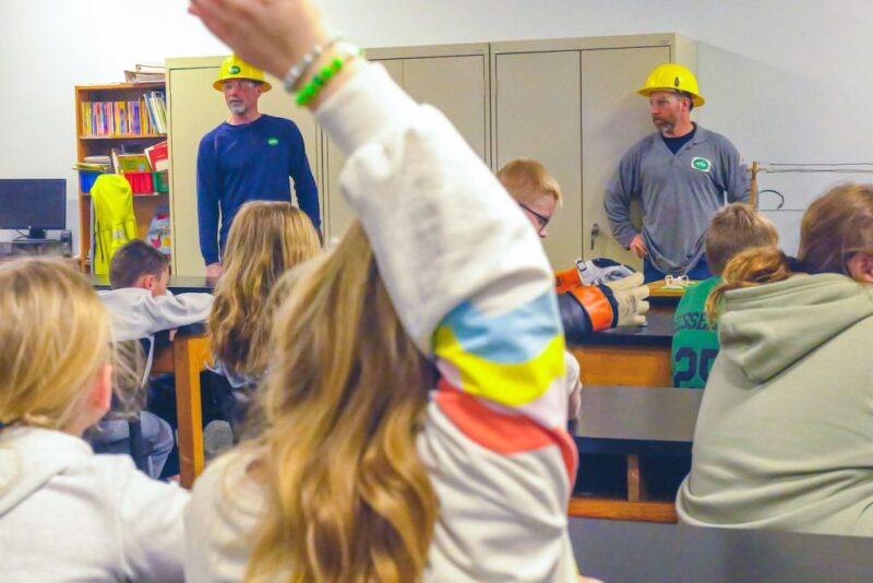 student raises hand while UPPCO representatives give a classroom presentation