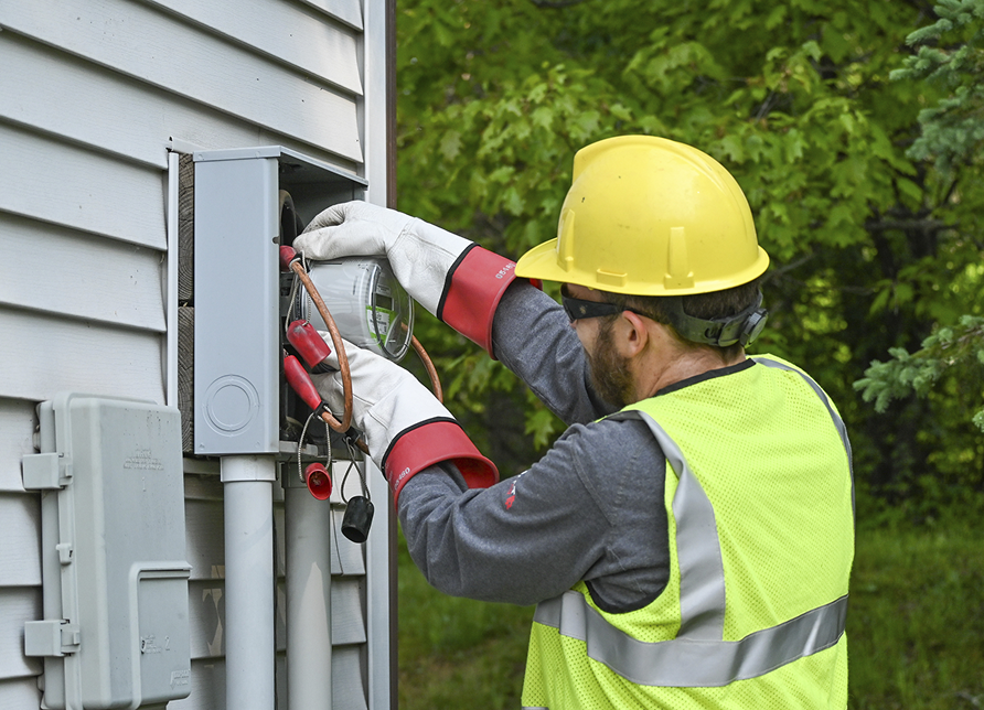 employee in high visibility gear, protective hard hat, and gloves works on a meter