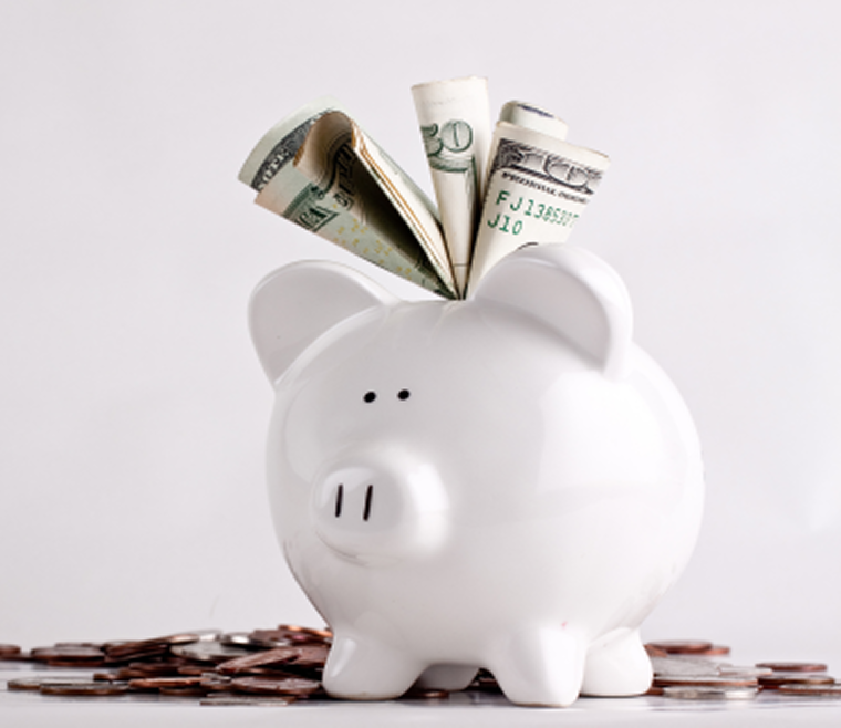 piggy bank with money stuffed in the top and coins sitting alongside