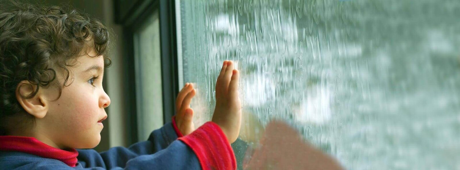 child looks out a window covered in rain
