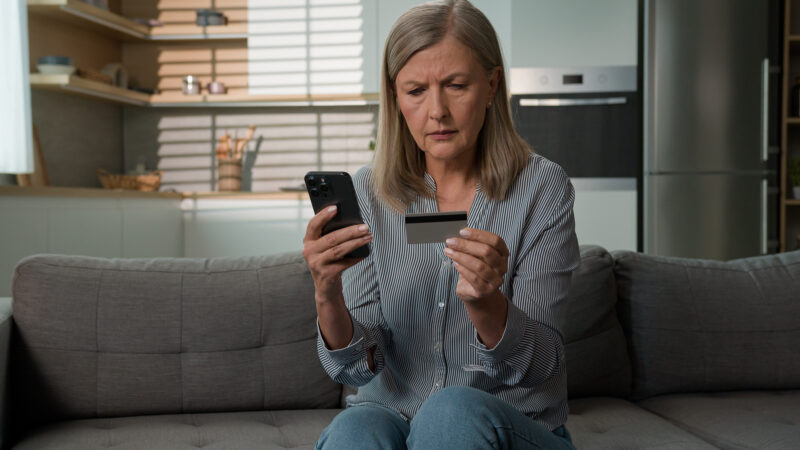 woman with a worried look holds her cellphone and a credit card