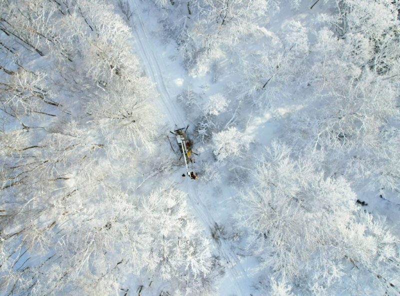 overhead view of a a snowy forest, vehicle tracks, and power line work underway